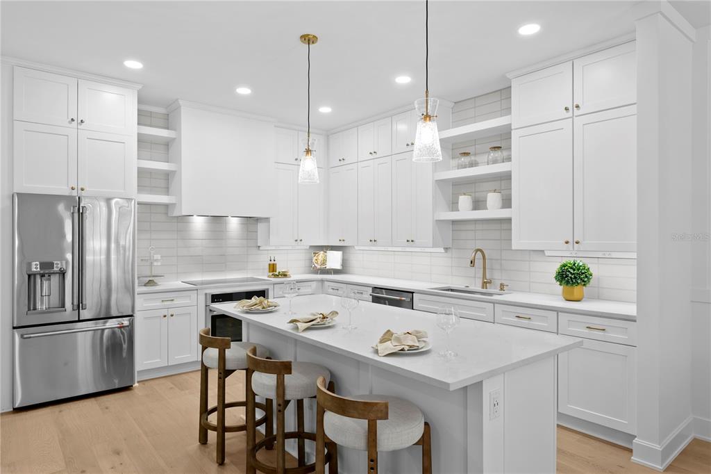 A modern white kitchen features a central island, stainless steel appliances, and light wood flooring — 450 GILMAN PLACE N, ST PETERSBURG, FL