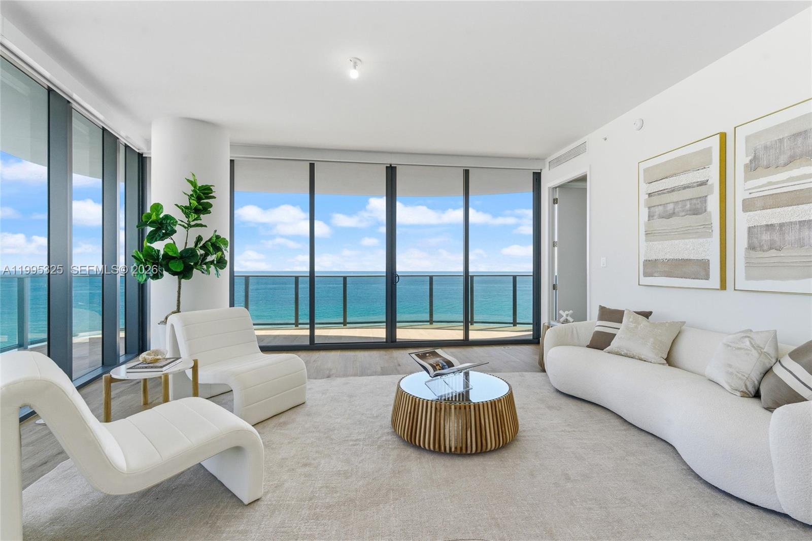 A modern living room features white furniture, a circular coffee table, and floor-to-ceiling ocean views — 900 N Ocean Blvd # 1506, Pompano Beach FL 33062, POMPANO BEACH, FL