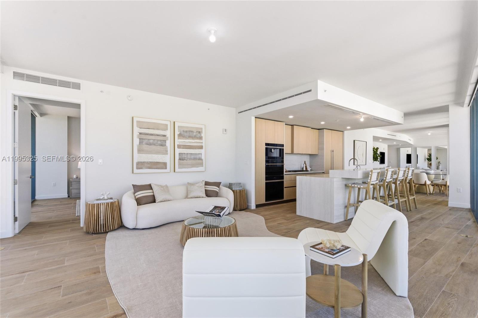 A modern open-concept living room and kitchen feature light wood floors and neutral furniture — 900 N Ocean Blvd # 1506, Pompano Beach FL 33062, POMPANO BEACH, FL
