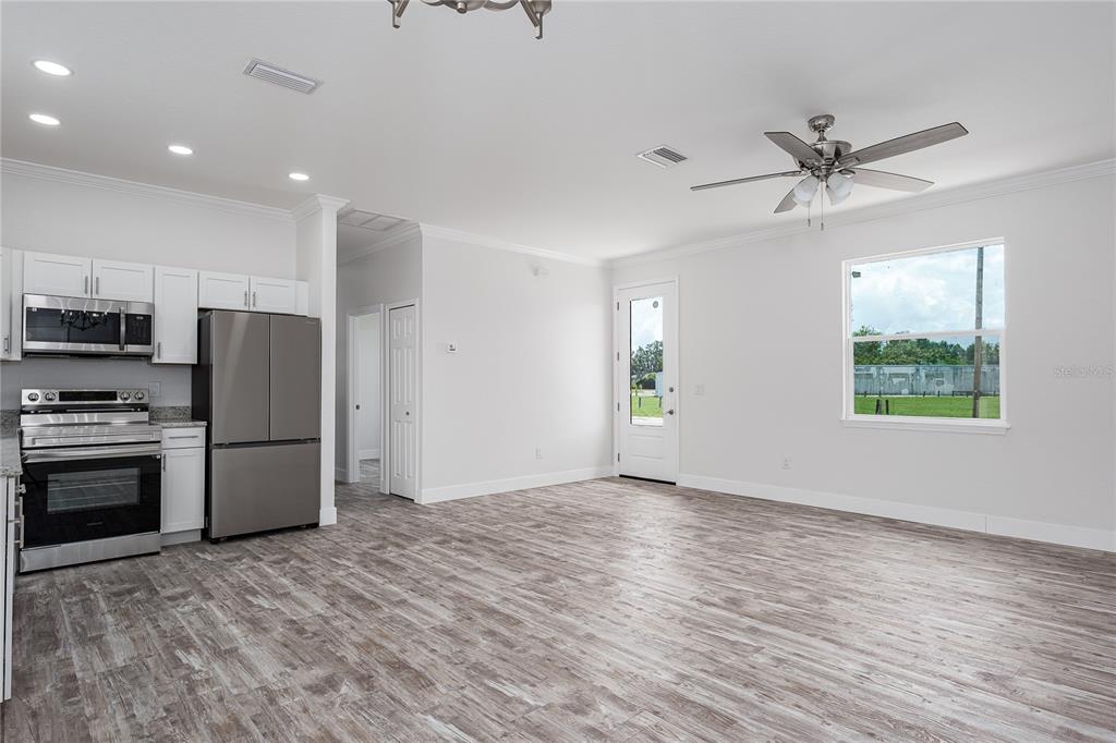 A kitchen with stainless steel appliances and white cabinets opens to a living area — 1515 2ND AVENUE W, PALMETTO, FL