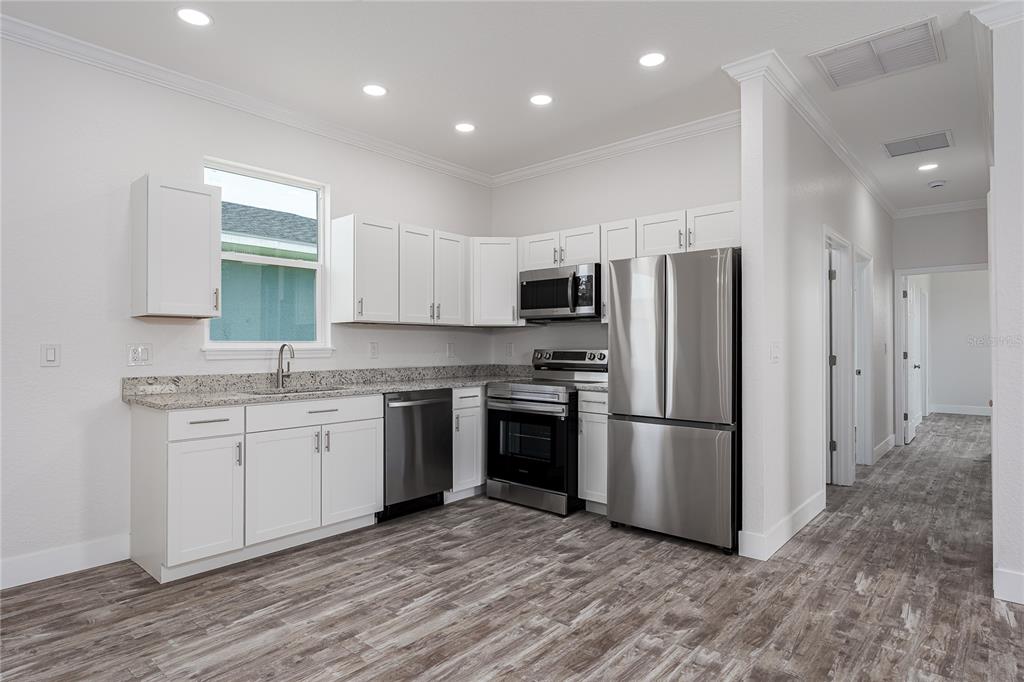 A modern kitchen features white cabinets, granite countertops, stainless steel appliances, and wood-look flooring — 1515 2ND AVENUE W, PALMETTO, FL