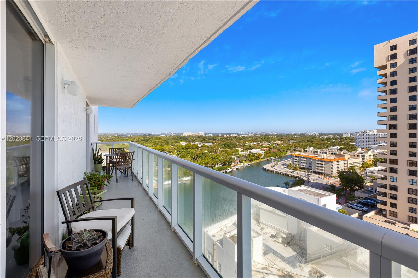 A high-rise balcony features outdoor furniture, a glass railing, and a view of a waterway — 2457 Collins Ave # 1602, Miami Beach FL 33140, MIAMI BEACH, FL