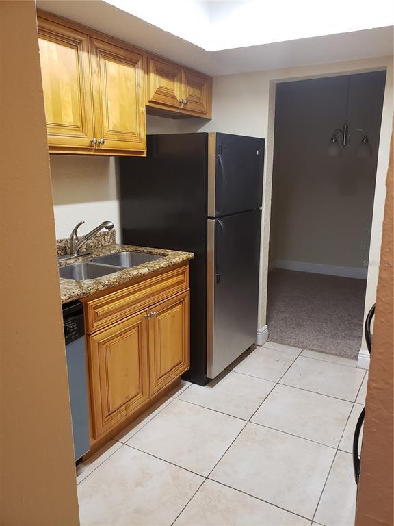 A kitchen features light wood cabinets, granite countertops, a black refrigerator, and tile flooring — 4801 S TEXAS AVENUE UNIT 4801D, ORLANDO, FL