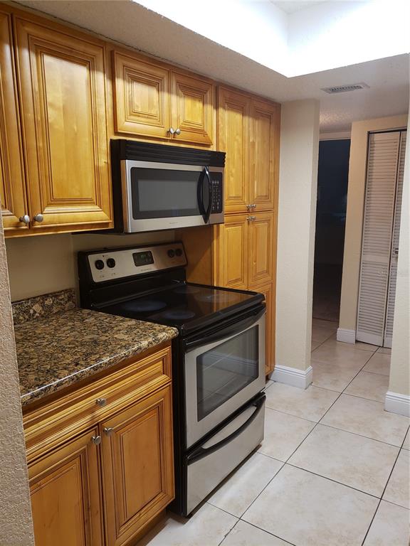 A kitchen features wood cabinets, granite countertops, and stainless steel appliances — 4801 S TEXAS AVENUE UNIT 4801D, ORLANDO, FL