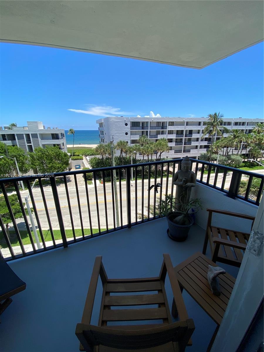 A balcony with a wooden chair and table overlooks a street, beach, and ocean — 531 N ocean # 611, Pompano Beach FL 33062, POMPANO BEACH, FL