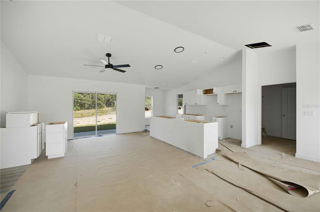 An unfinished kitchen and living area features white cabinets, a center island, and sliding doors — 1690 SW VIBURNUM ROAD, DUNNELLON, FL