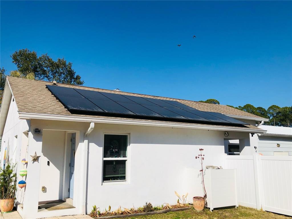 A white house exterior features a large solar panel array mounted on the shingled roof — 405 CONNECTICUT AVENUE, FLAGLER BEACH, FL