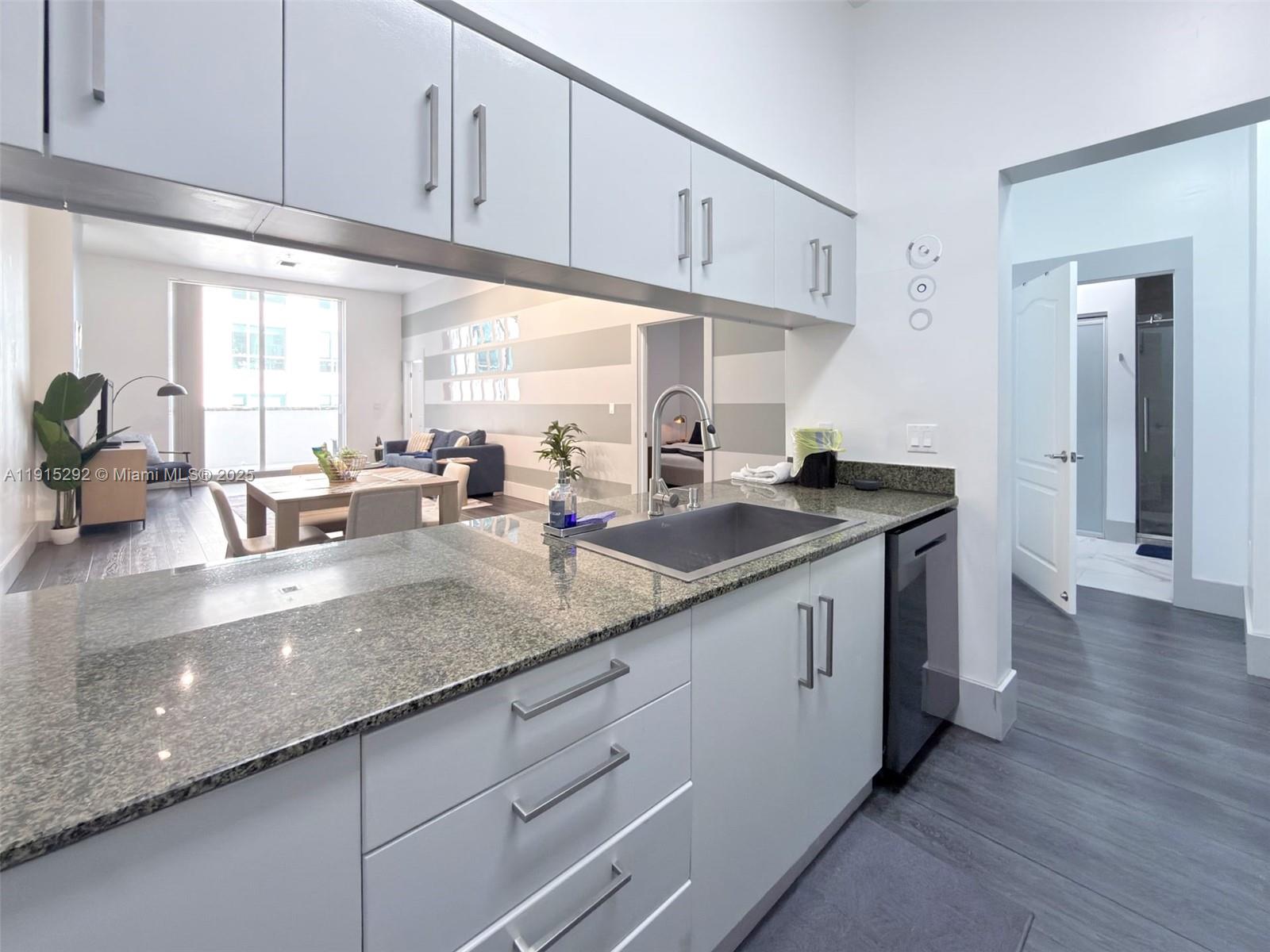 A kitchen features gray cabinets, granite countertops, a sink, and a view into the living area — 1200 Brickell Bay Dr # 1406, Miami FL 33131, MIAMI, FL