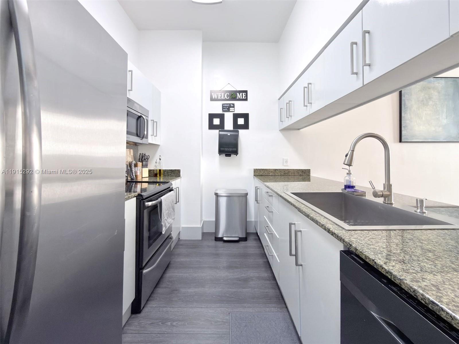 A galley kitchen features white cabinets, granite countertops, stainless steel appliances, and gray wood-look flooring — 1200 Brickell Bay Dr # 1406, Miami FL 33131, MIAMI, FL