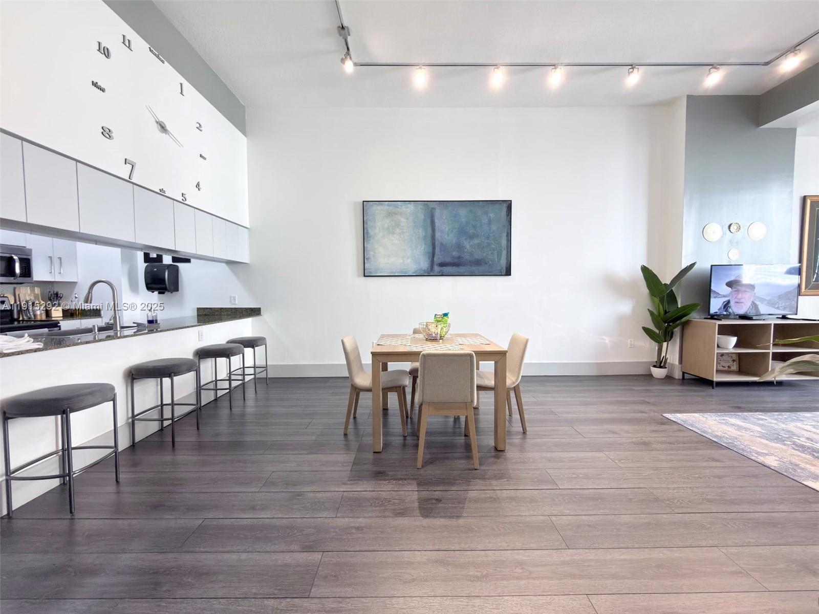 A modern open-concept living and dining area features dark wood floors and a wall clock — 1200 Brickell Bay Dr # 1406, Miami FL 33131, MIAMI, FL
