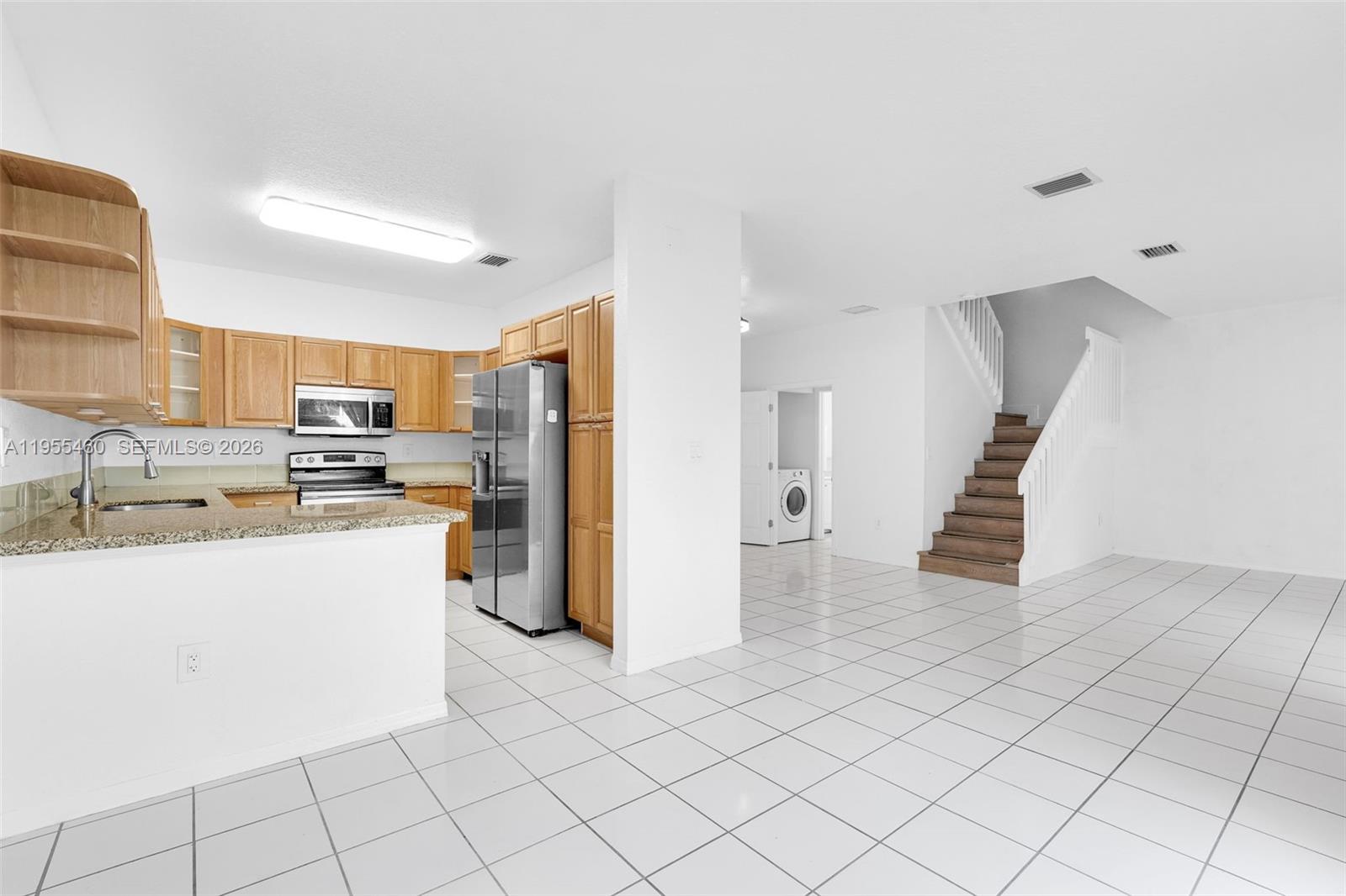A kitchen with wood cabinets and granite countertops opens to a tiled living area — 1120 Cliffrose St, Hollywood FL 33019, HOLLYWOOD, FL