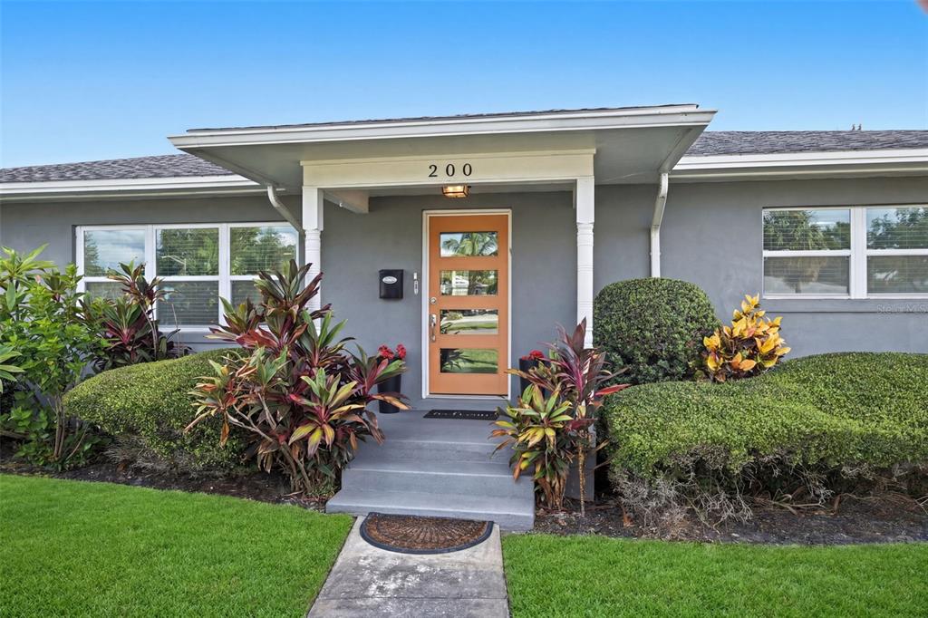 A gray house exterior features a light orange front door with glass panels and landscaping — 200 PARK STREET N, ST PETERSBURG, FL