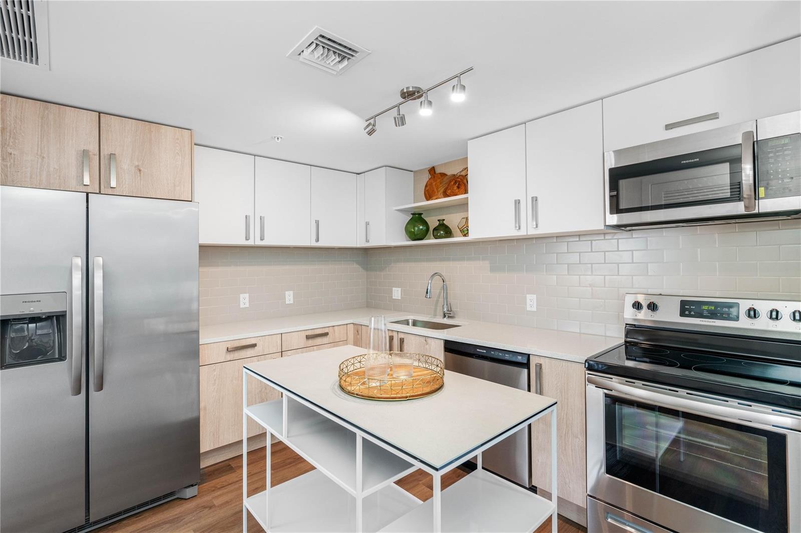 A modern kitchen features white and wood-tone cabinets, stainless steel appliances, and a central island — 200 NE 1st Avenue # 1027, Pompano Beach FL 33060, POMPANO BEACH, FL