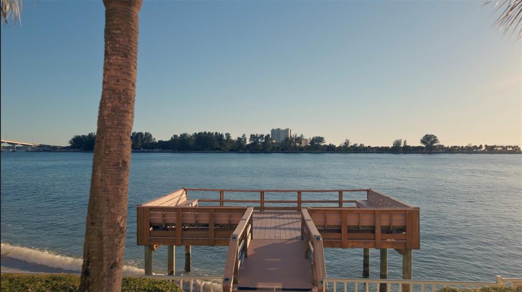 A wooden deck with built-in benches extends over the water toward a distant bridge — 675 S GULFVIEW BOULEVARD UNIT 606, CLEARWATER BEACH, FL