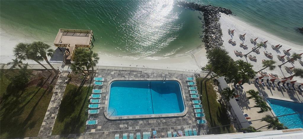 An aerial view shows a swimming pool, lounge chairs, and a beach with a wooden deck — 675 S GULFVIEW BOULEVARD UNIT 606, CLEARWATER BEACH, FL