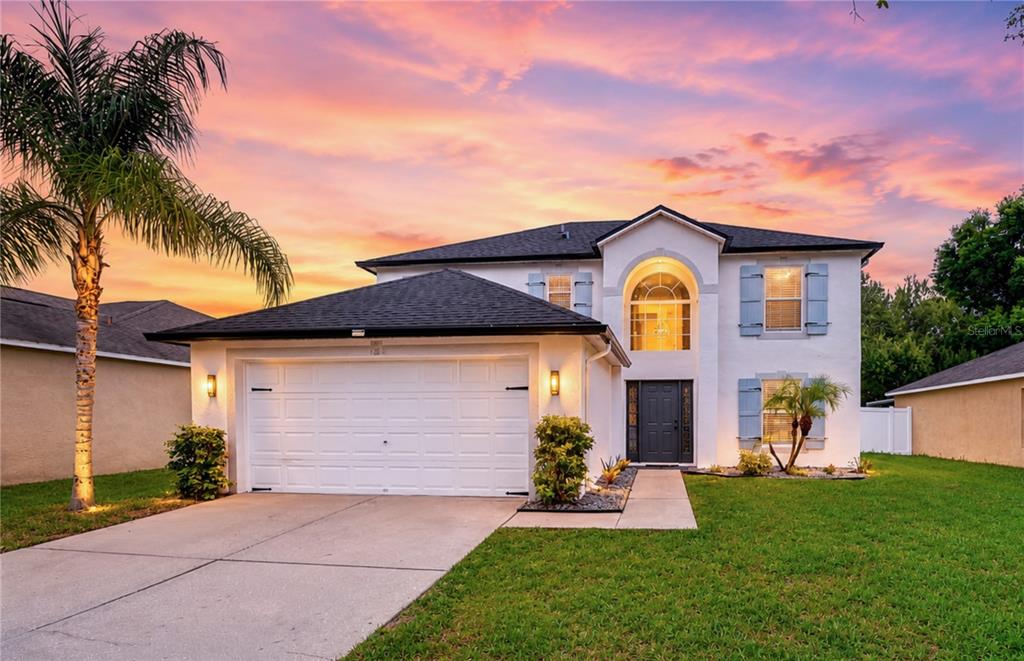 A two-story white house with a two-car garage and a palm tree at sunset — 12928 KINGS LAKE DRIVE, GIBSONTON, FL