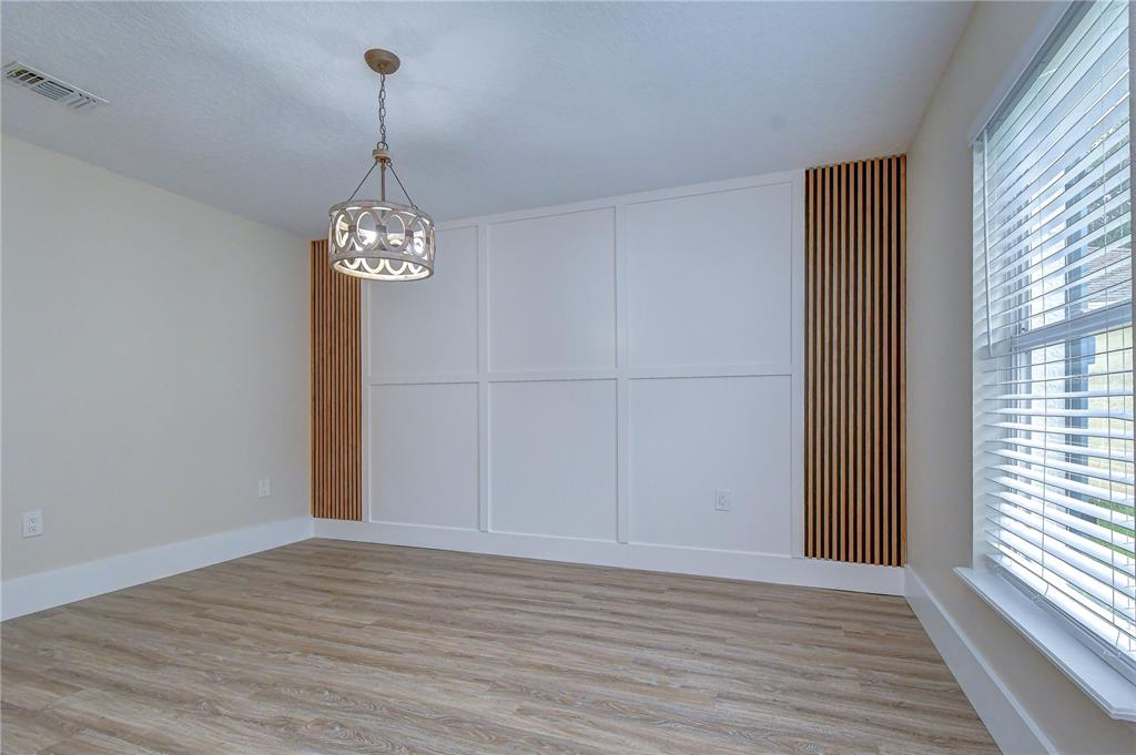 An empty dining room features light wood-look flooring, a chandelier, and a white paneled accent wall — 12928 KINGS LAKE DRIVE, GIBSONTON, FL