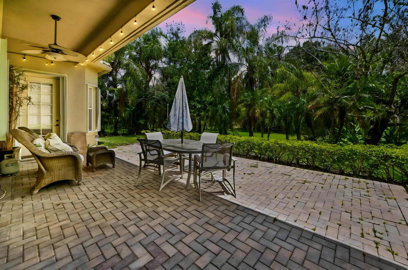 A paved patio features a dining set with an umbrella and wicker lounge chairs — 1488 SE Legacy Cove Circle, Stuart FL 34997, STUART, FL