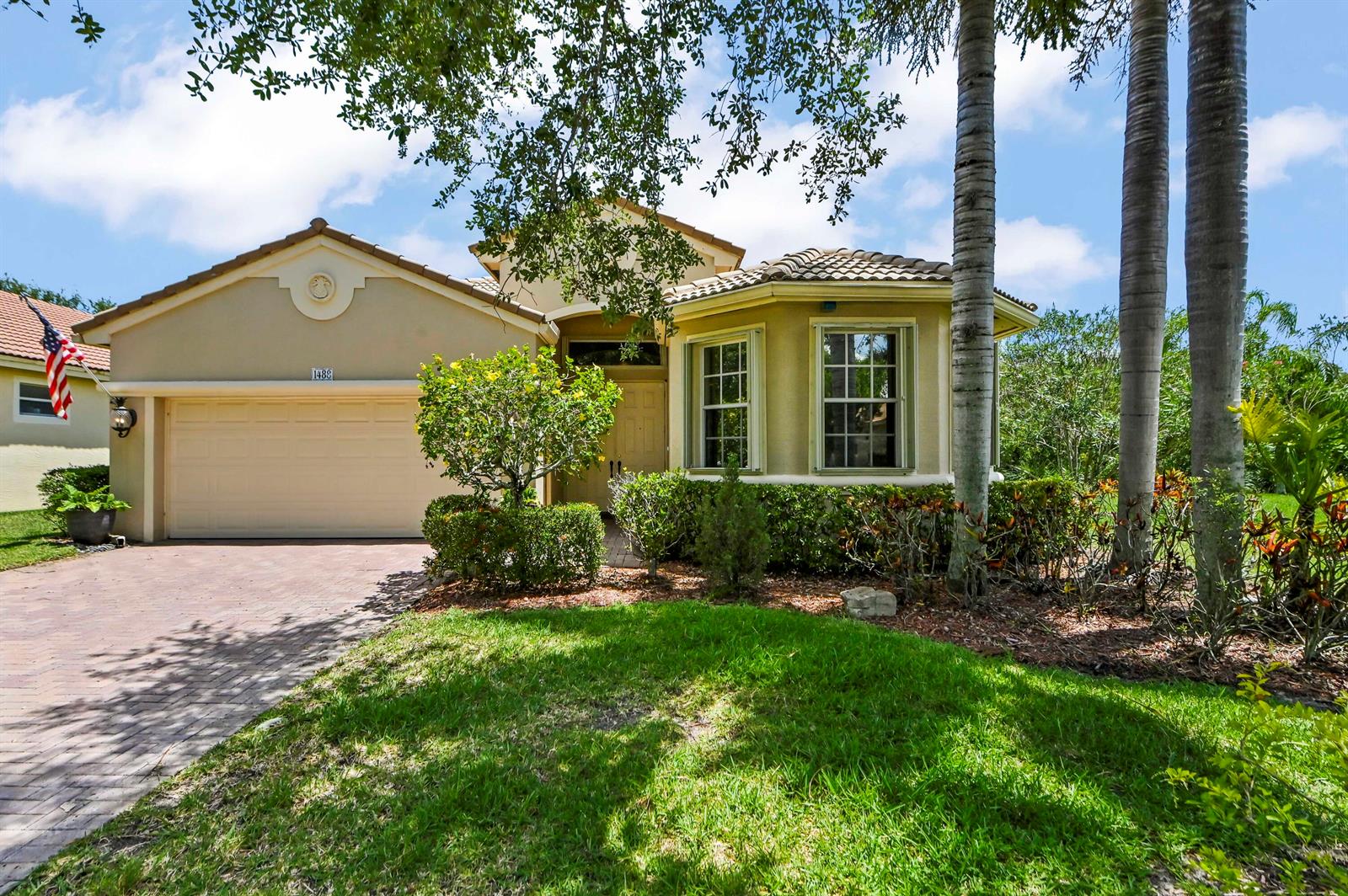 A tan single-story house with a two-car garage, tile roof, and palm trees in front — 1488 SE Legacy Cove Circle, Stuart FL 34997, STUART, FL