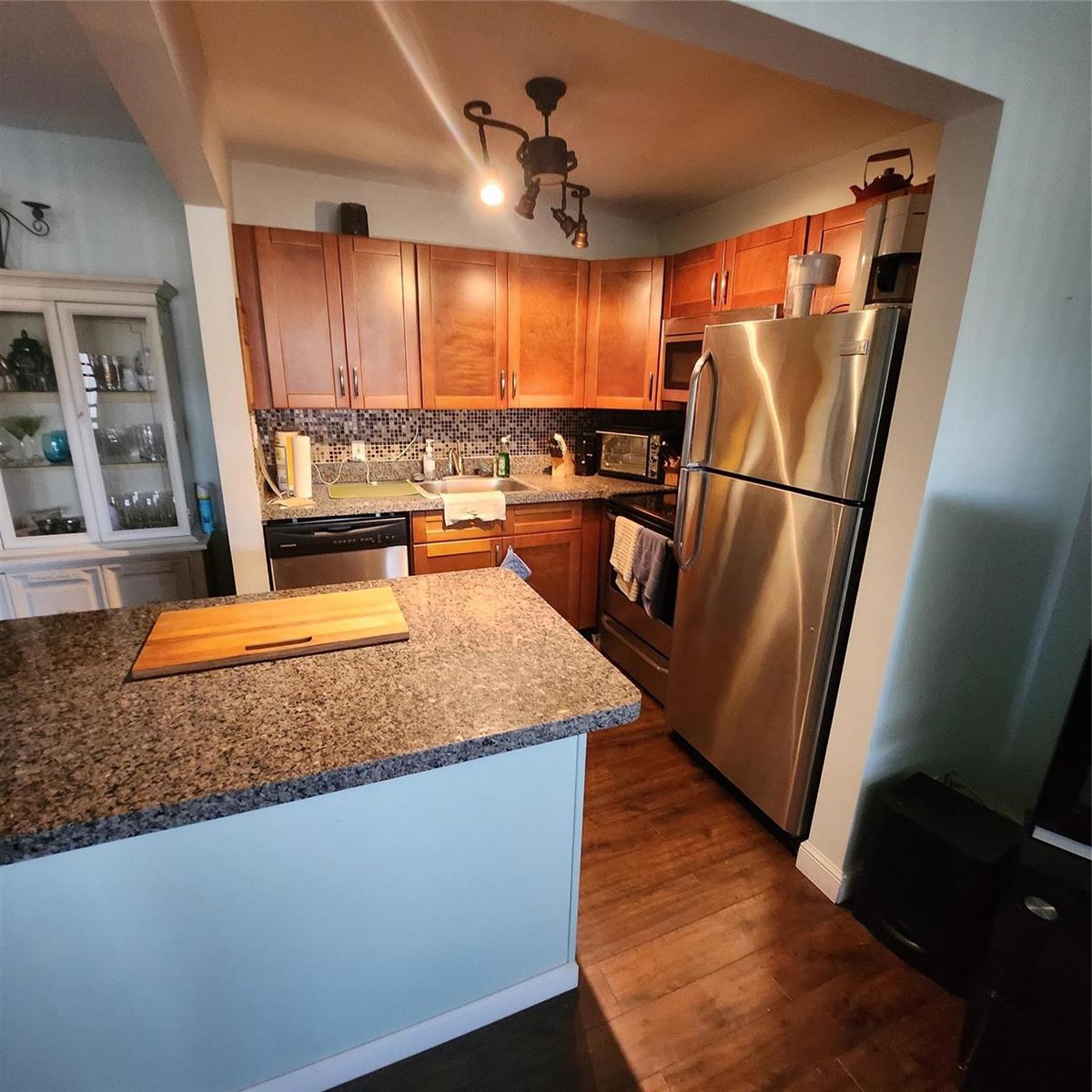 A kitchen features wood cabinets, granite countertops, stainless steel appliances, and a central island — 198 Durham D, Deerfield Beach FL 33442, DEERFIELD BEACH, FL