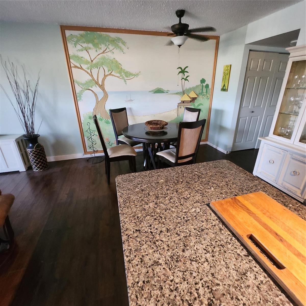 A dining area features a large wall mural, a round table with chairs, and dark flooring — 198 Durham D, Deerfield Beach FL 33442, DEERFIELD BEACH, FL