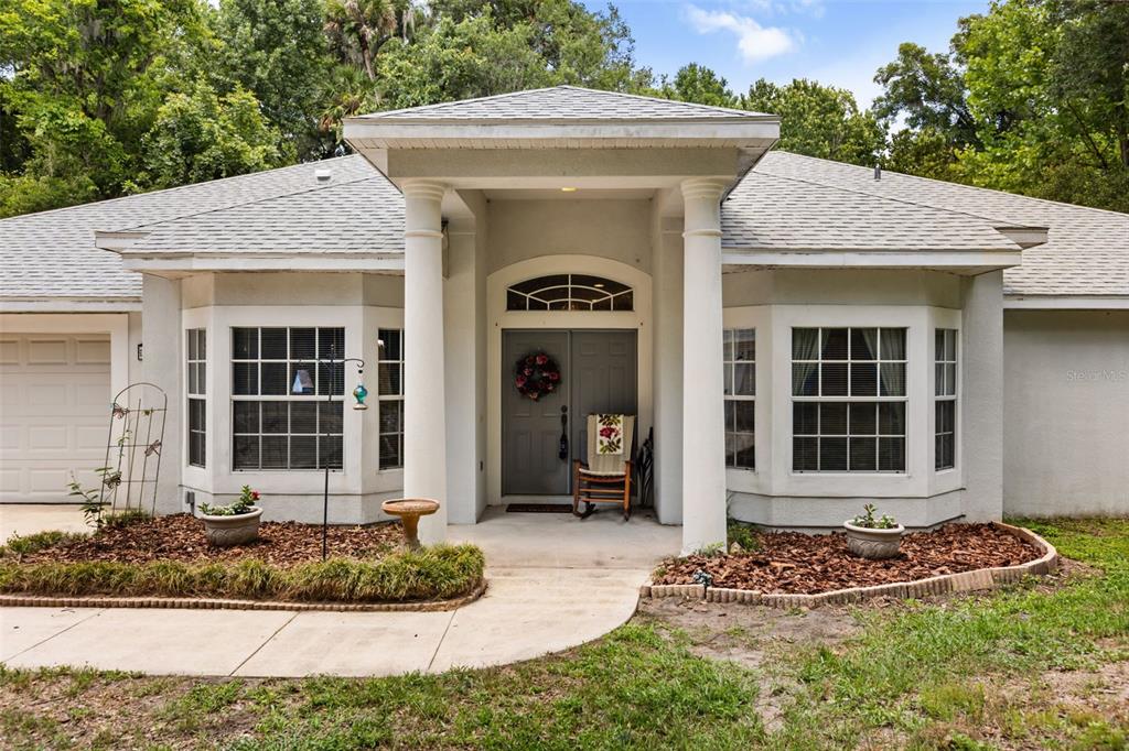 A single-story house exterior features a covered entryway with two white columns and a gray door — 1420 MIRKWOOD COVE, OVIEDO, FL