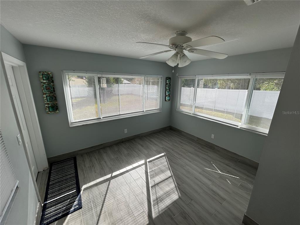 A sunroom features light gray wood-look tile flooring, white walls, and large windows with blinds — 21570 SW RAINTREE STREETS, DUNNELLON, FL