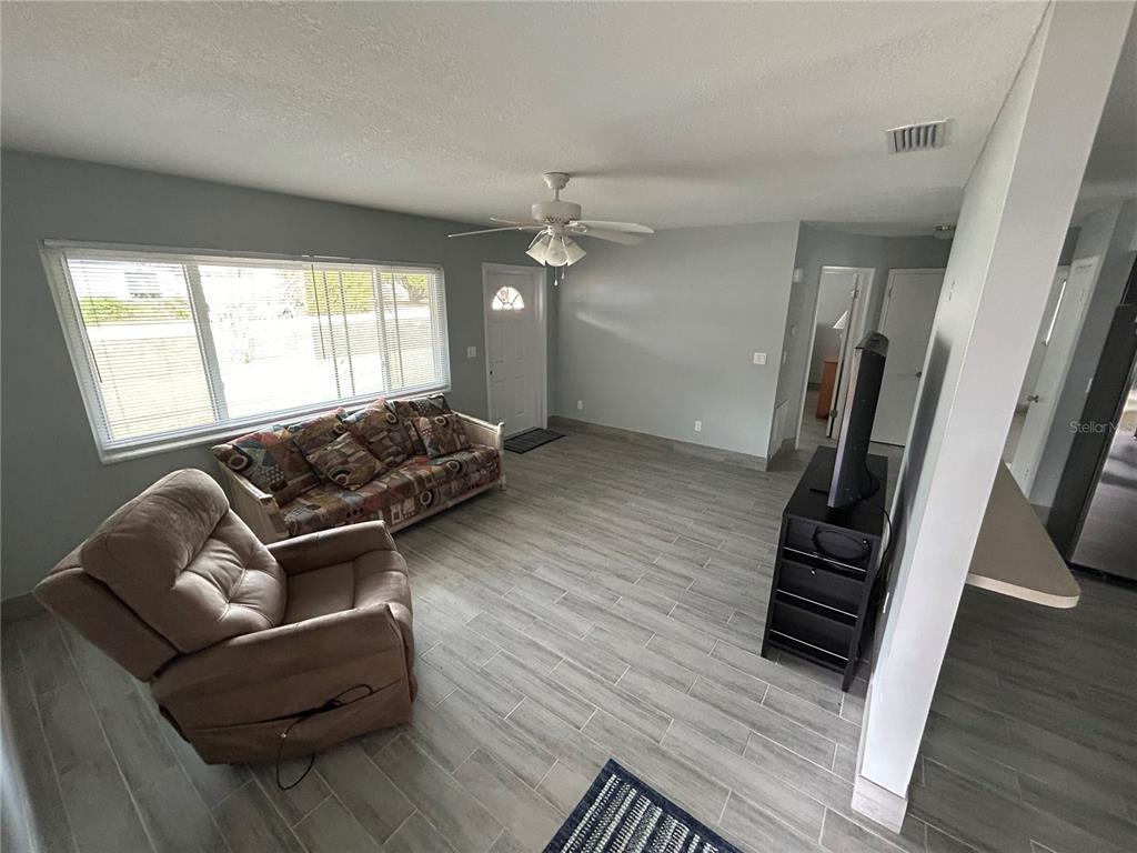A living room features gray wood-look tile flooring, a ceiling fan, and a large window — 21570 SW RAINTREE STREETS, DUNNELLON, FL