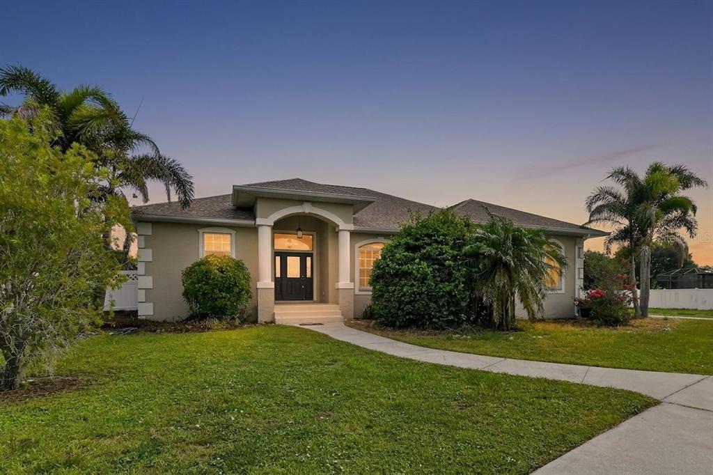 A single-story house with a beige stucco exterior, arched entryway, and palm trees at dusk — 16323 UPPER MANATEE RIVER ROAD, BRADENTON, FL