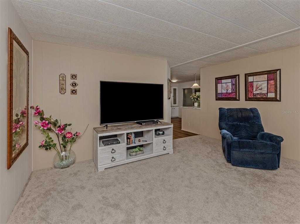 A living room features beige walls, carpeted flooring, a television console, and a blue recliner — 222 SCHOONER STREET, NORTH PORT, FL