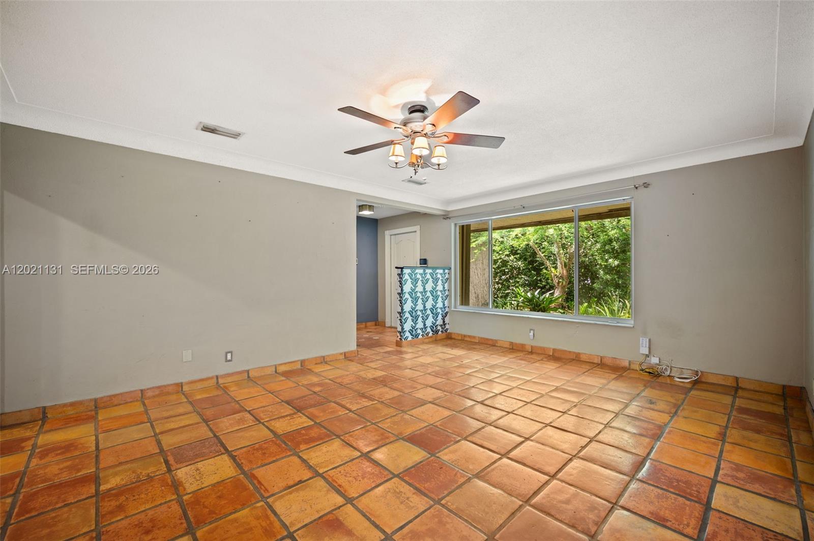 An empty room features terracotta tile flooring, a ceiling fan, and a large picture window — 4512 SW 37th Ave, Dania Beach FL 33312, DANIA BEACH, FL