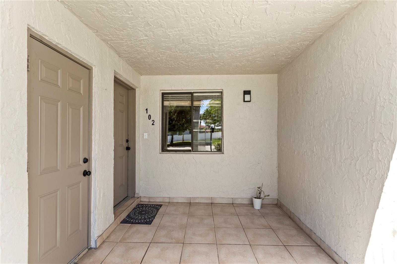 A covered entryway features a tiled floor, two beige doors, and a window with house number 102 — 16211 Saddle Club Road # 102, Weston FL 33326, WESTON, FL