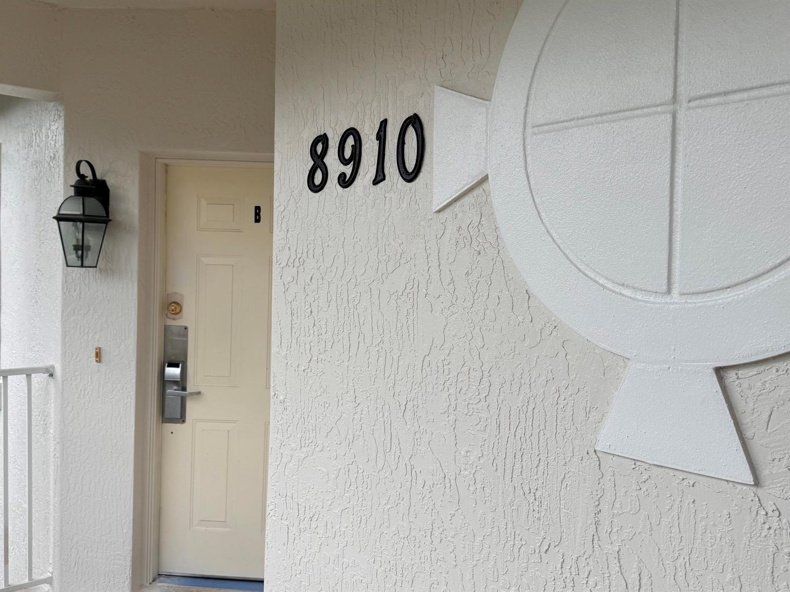 A white exterior wall features the number 8910, a decorative circular emblem, and a door labeled B — 8910 Sandshot Court # 5123, FL 34986, FL
