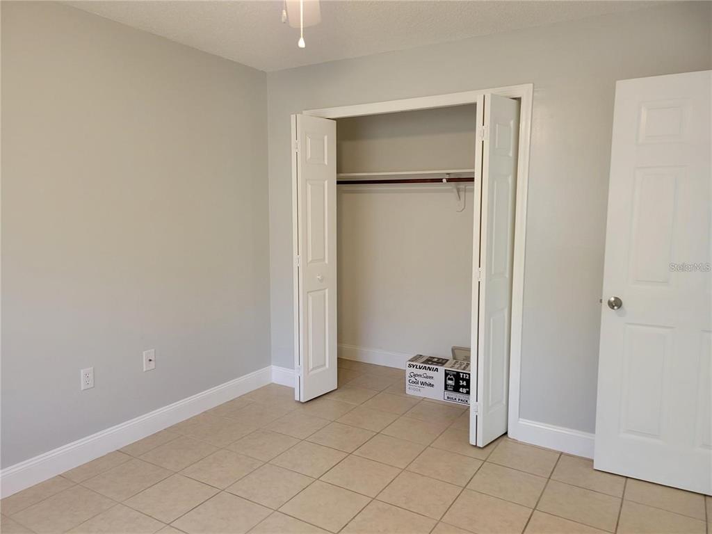 A bedroom with light gray walls, tile flooring, a white closet, and a white door — 807 MCLAIN COURT, TAVARES, FL