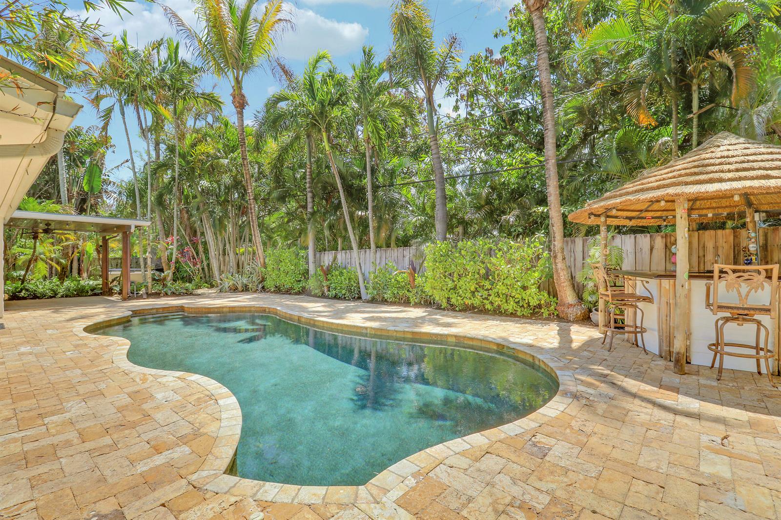 A backyard swimming pool with a stone patio and a thatched-roof tiki bar — 19931 Jasmine Drive, Jupiter FL 33469, JUPITER, FL