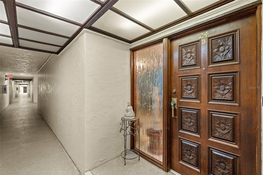 A wooden door with carved floral panels sits beside a textured glass sidelight in a hallway — 3035 COUNTRYSIDE BOULEVARD UNIT 24B, CLEARWATER, FL