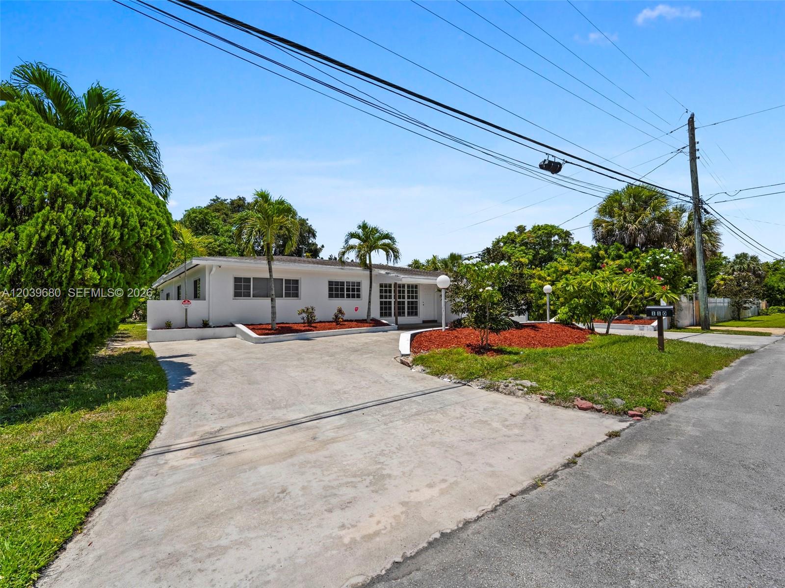 A single-story white house with a concrete driveway and palm trees under a blue sky — 110 NE 152nd St, Miami FL 33162, MIAMI, FL
