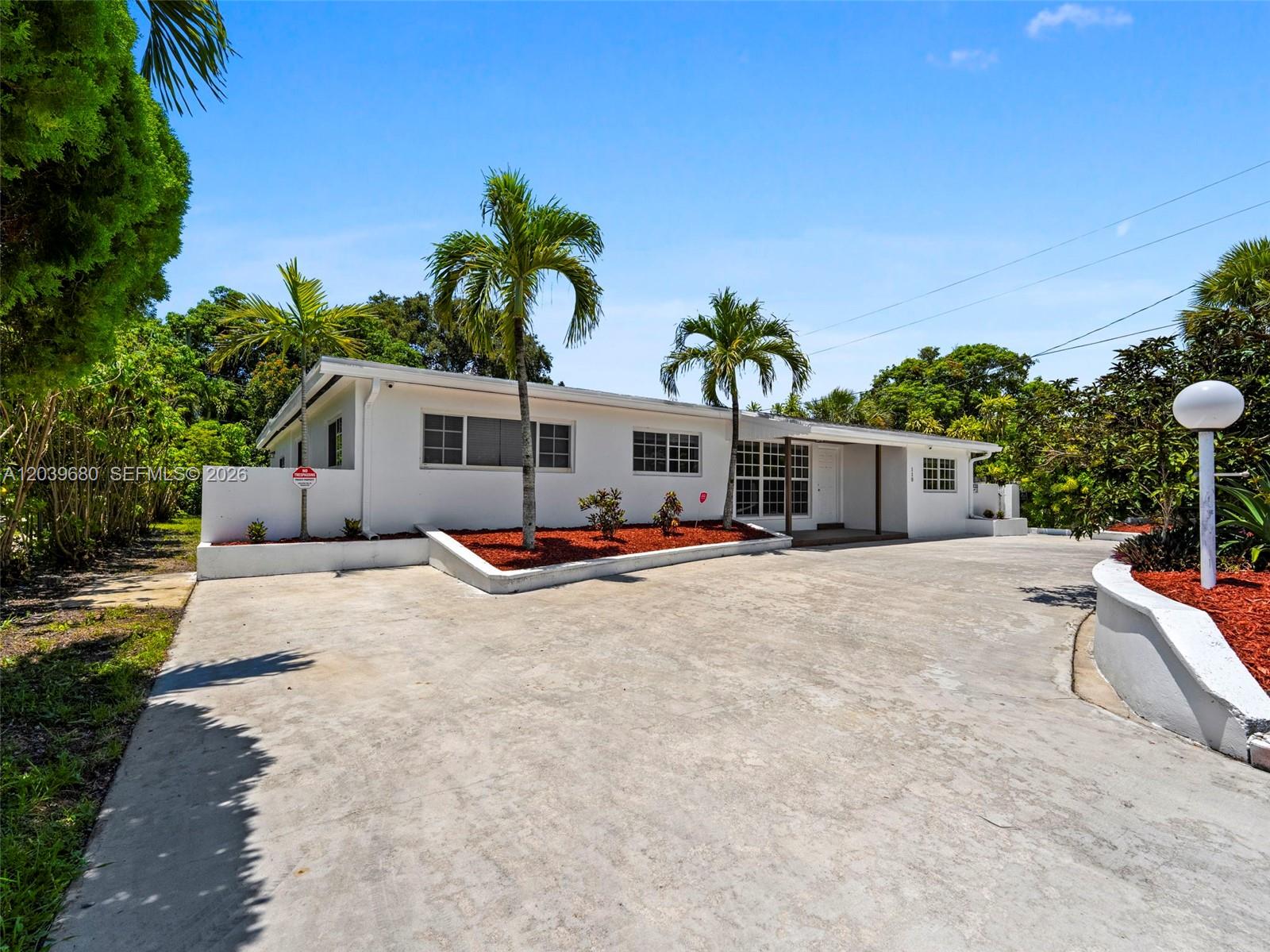 A white single-story house features a large concrete driveway and several palm trees — 110 NE 152nd St, Miami FL 33162, MIAMI, FL