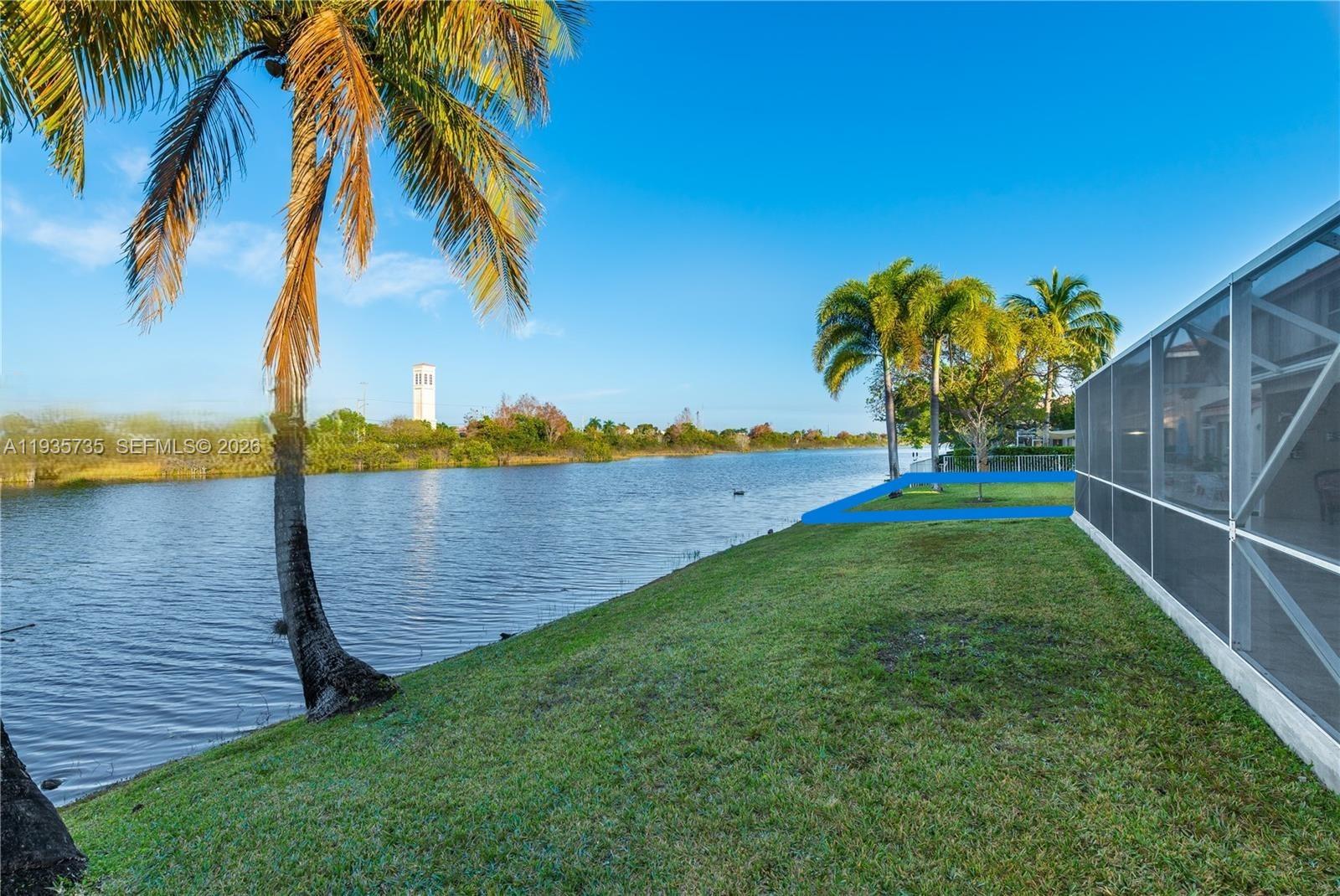 A grassy backyard slopes down to a lake next to a screened-in patio — 2824 SW 183rd Ave, Miramar FL 33029, MIRAMAR, FL