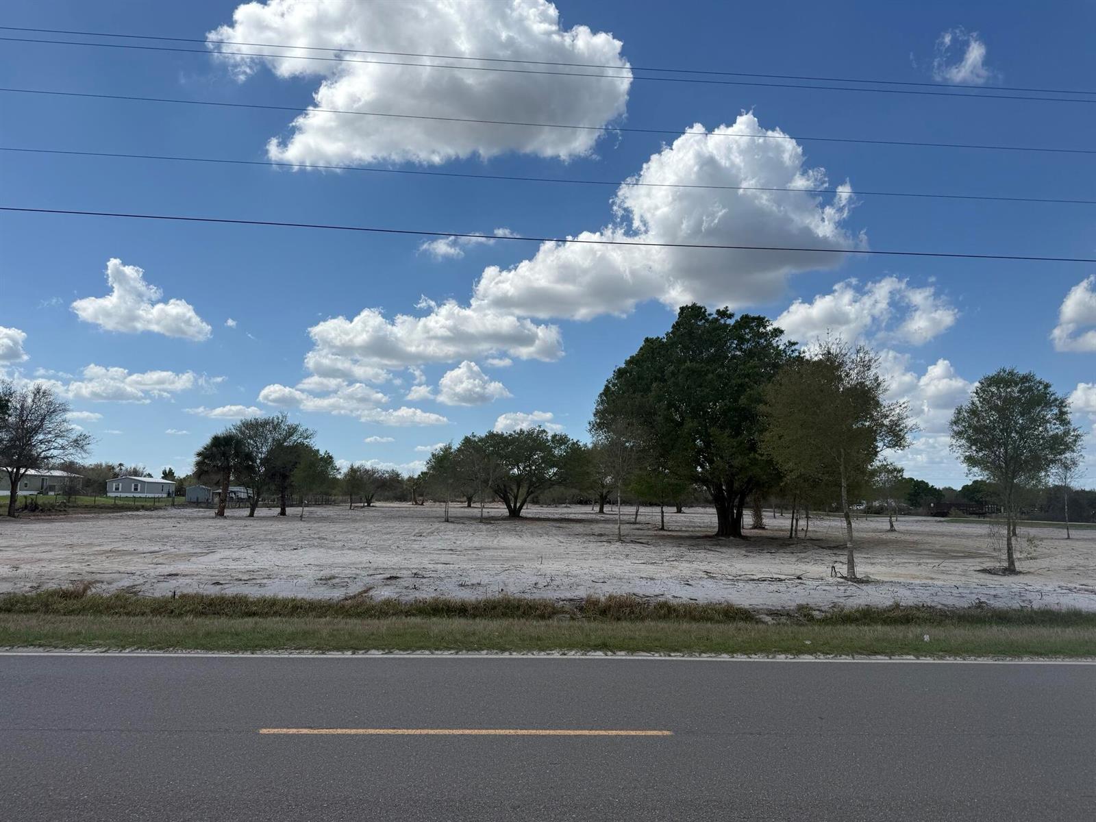 A wide, cleared, sandy lot with scattered trees sits alongside a paved road — 14416 NW 252nd Street, Okeechobee FL 34972, OKEECHOBEE, FL