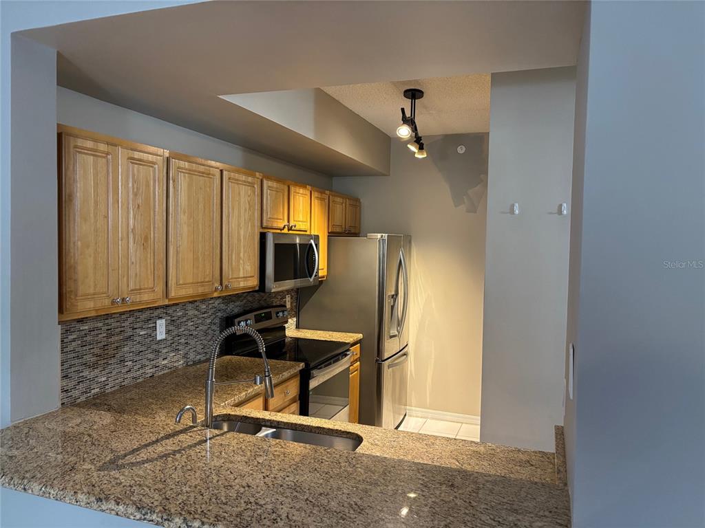 A kitchen with granite countertops, wooden cabinets, stainless steel appliances, and a mosaic tile backsplash — 5691 BENTGRASS DRIVE UNIT 15-209, SARASOTA, FL