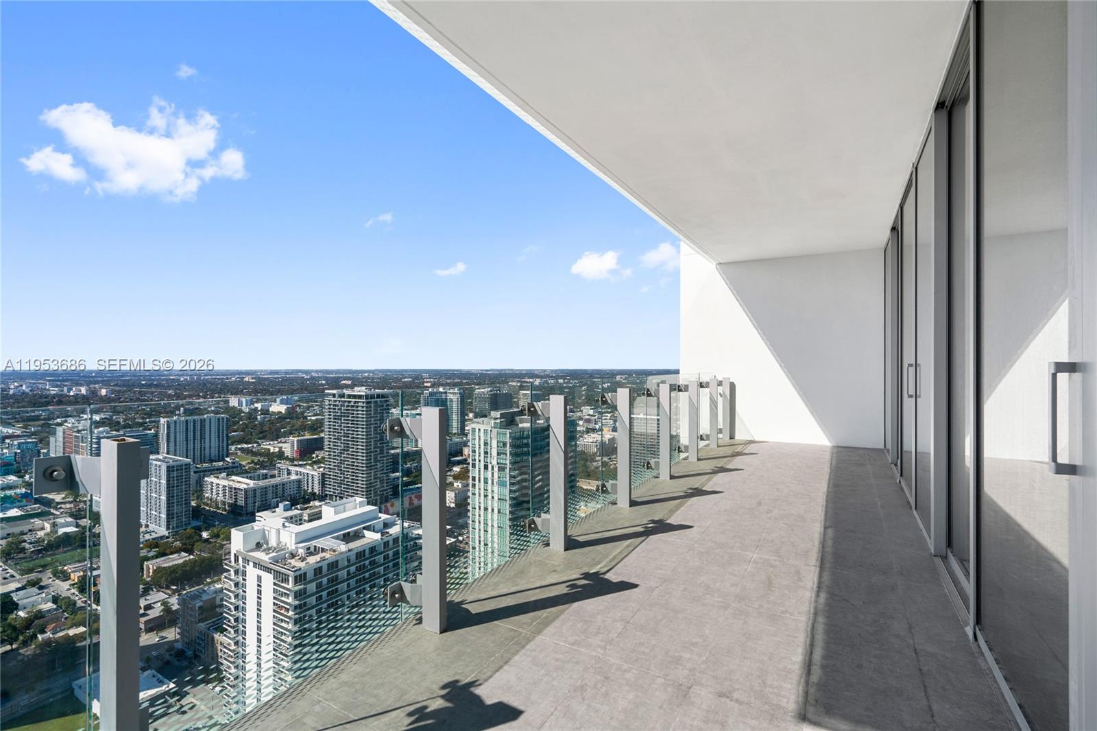 A high-rise balcony features gray tiled flooring, glass railings, and expansive city views — 700 NE 26th Ter # 4903, Miami FL 33137, MIAMI, FL