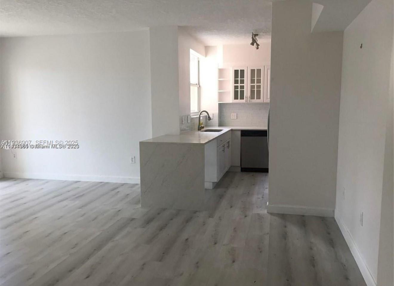 An open-concept kitchen features white cabinets, a marble-patterned peninsula, and light wood-look flooring — 1824 Brickell Ave # 2B, Miami FL 33129, MIAMI, FL