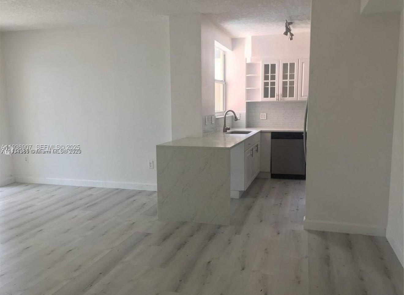 A kitchen with white cabinets and a marble-topped peninsula overlooks a light-floored living area — 1824 Brickell Ave # 2B, Miami FL 33129, MIAMI, FL