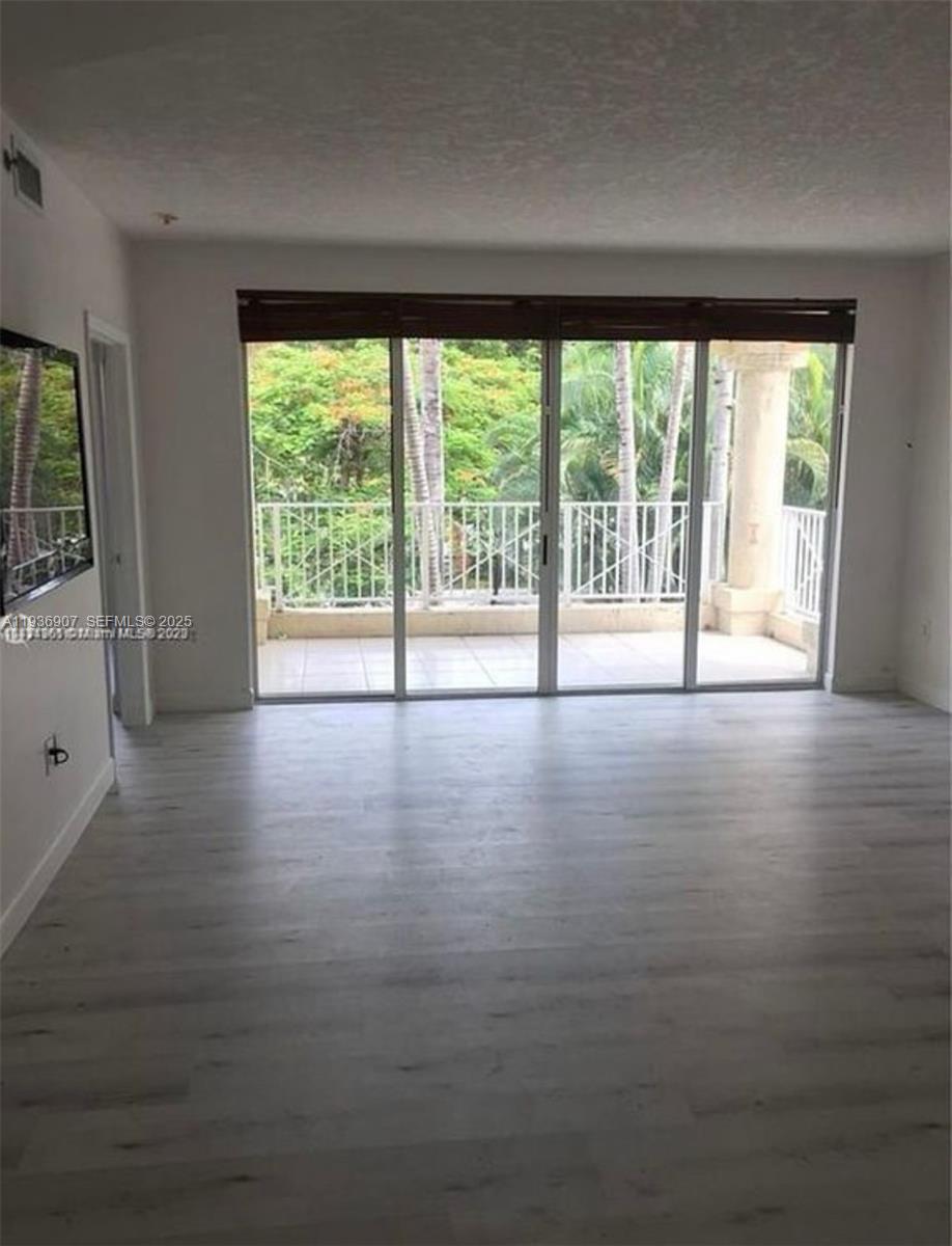 An empty room with light wood-look flooring features a large sliding glass door to a balcony — 1824 Brickell Ave # 2B, Miami FL 33129, MIAMI, FL