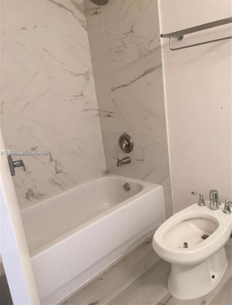 A bathroom features a white bathtub with marble-style tile walls and a white bidet — 1824 Brickell Ave # 2B, Miami FL 33129, MIAMI, FL