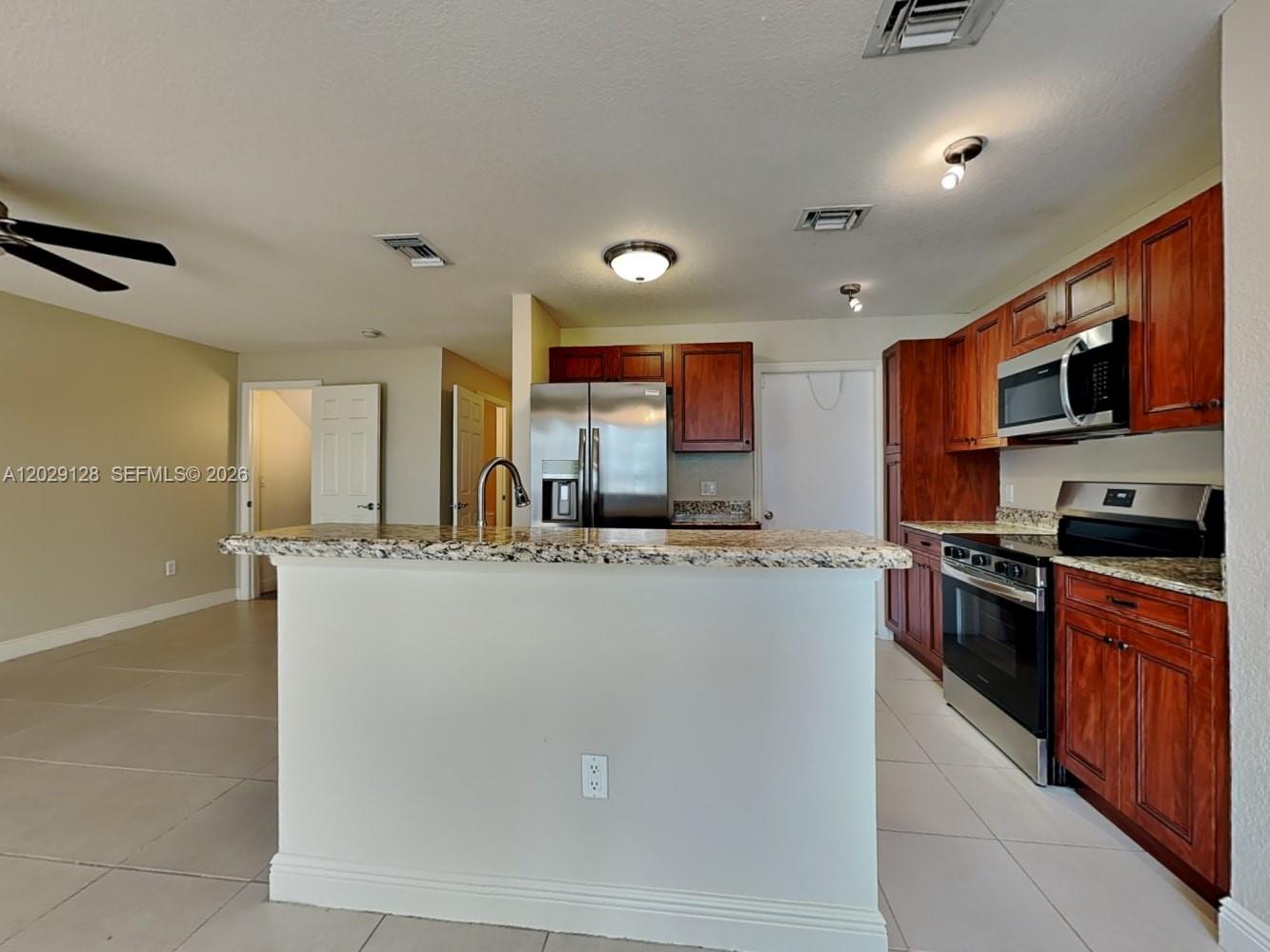 A kitchen features wood cabinets, granite countertops, stainless steel appliances, and a central island — BOYNTON BEACH, FL