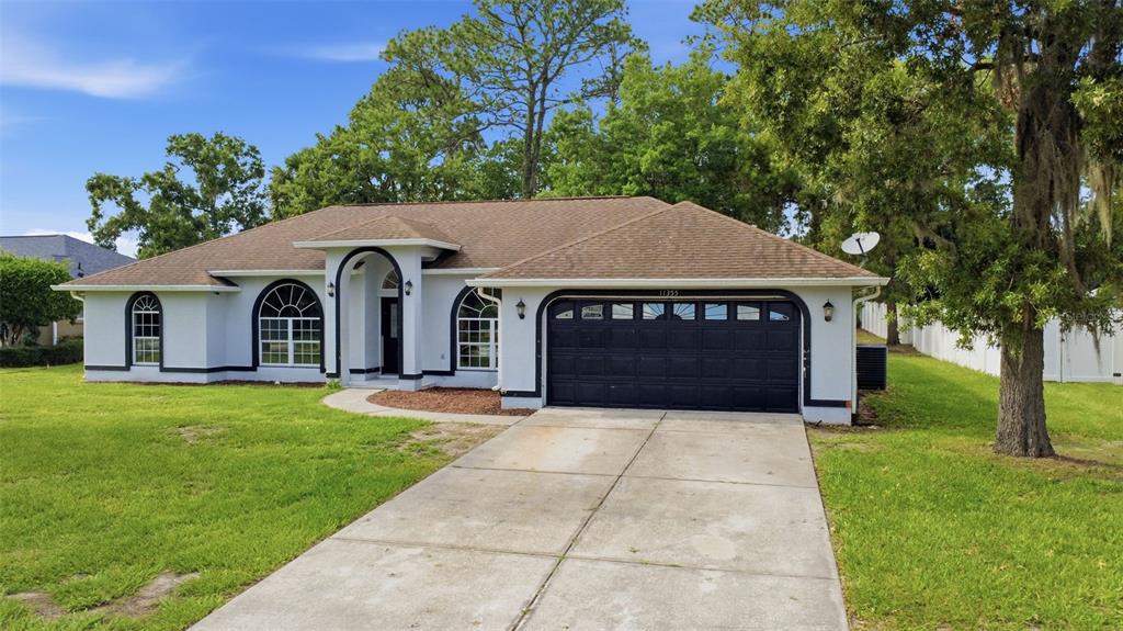 A single-story house with a brown roof, white stucco walls, and a black garage door — 11355 SW 58TH CIRCLE, OCALA, FL