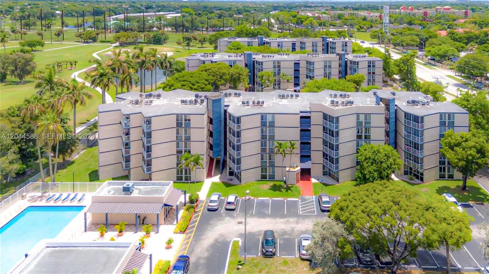 An aerial view shows a swimming pool, a clubhouse, and apartment buildings next to a golf course — 7035 NW 186th St # D110, Hialeah FL 33015, HIALEAH, FL