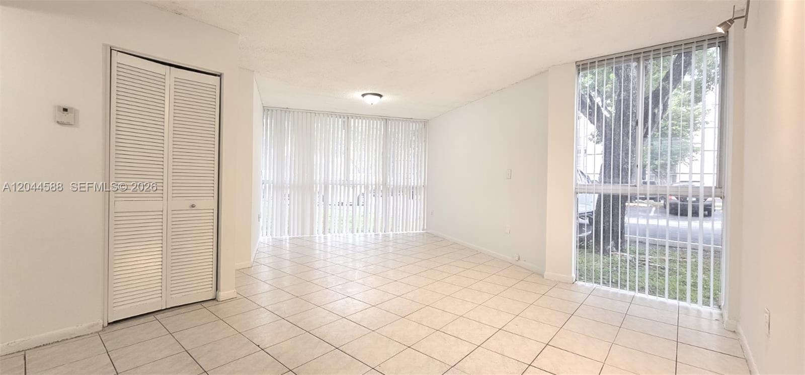 An empty room features white tile flooring, a closet with louvered doors, and floor-to-ceiling windows — 7035 NW 186th St # D110, Hialeah FL 33015, HIALEAH, FL
